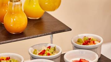 A hand reaching for a light bulb-shaped glass with a yellow liquid, surrounded by similar glasses and small bowls with fruit toppings.