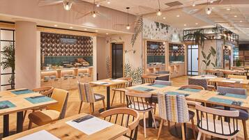 A modern restaurant with wooden tables and chairs, a counter with food displays, and decorative plant wall art.