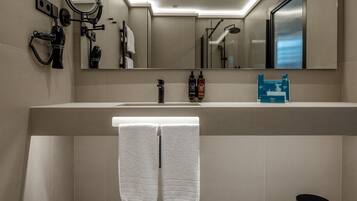 A modern bathroom with a large mirror, a towel rack with two towels, a sink, and a black trash can.