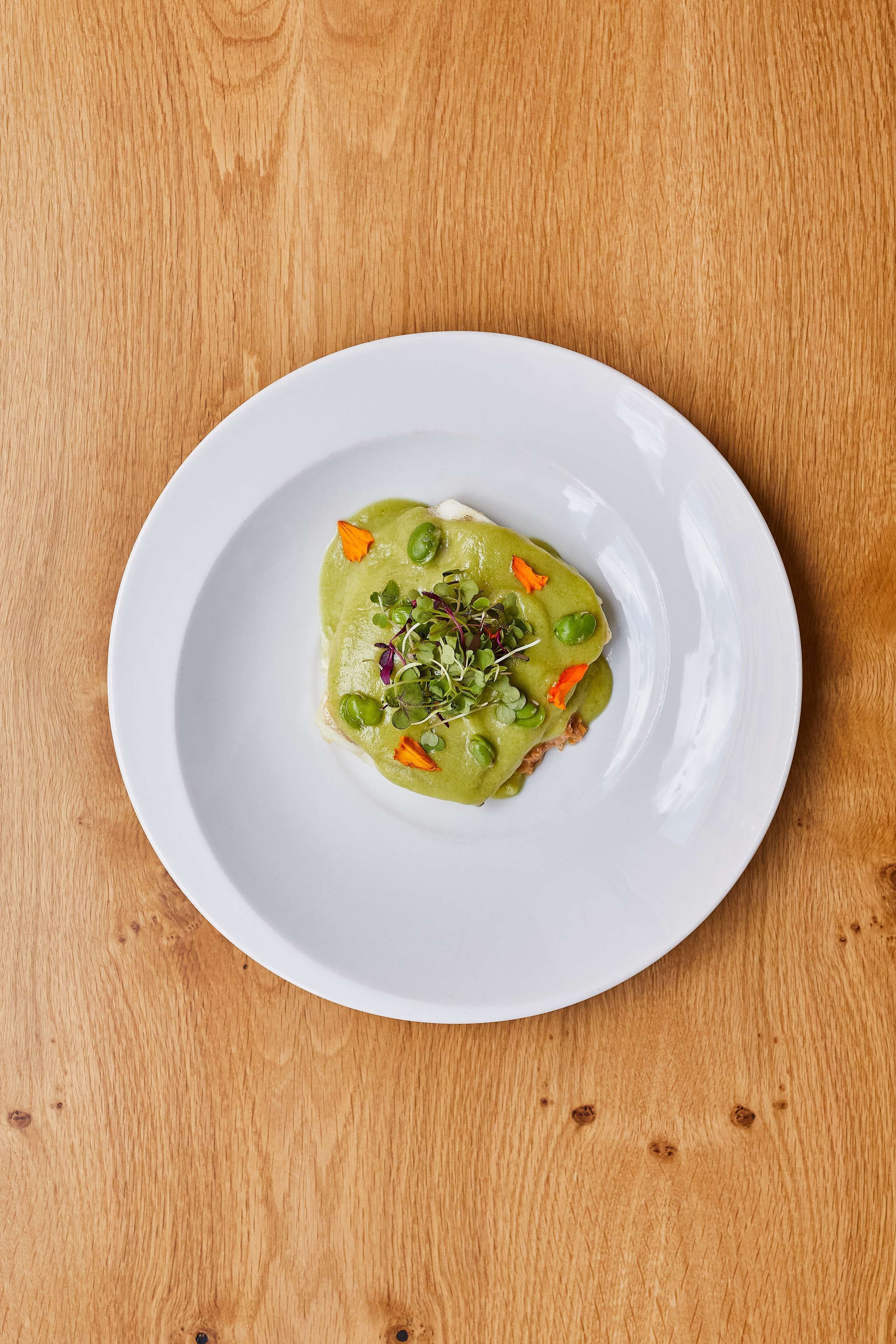 A white plate with a green dish on a wooden table.