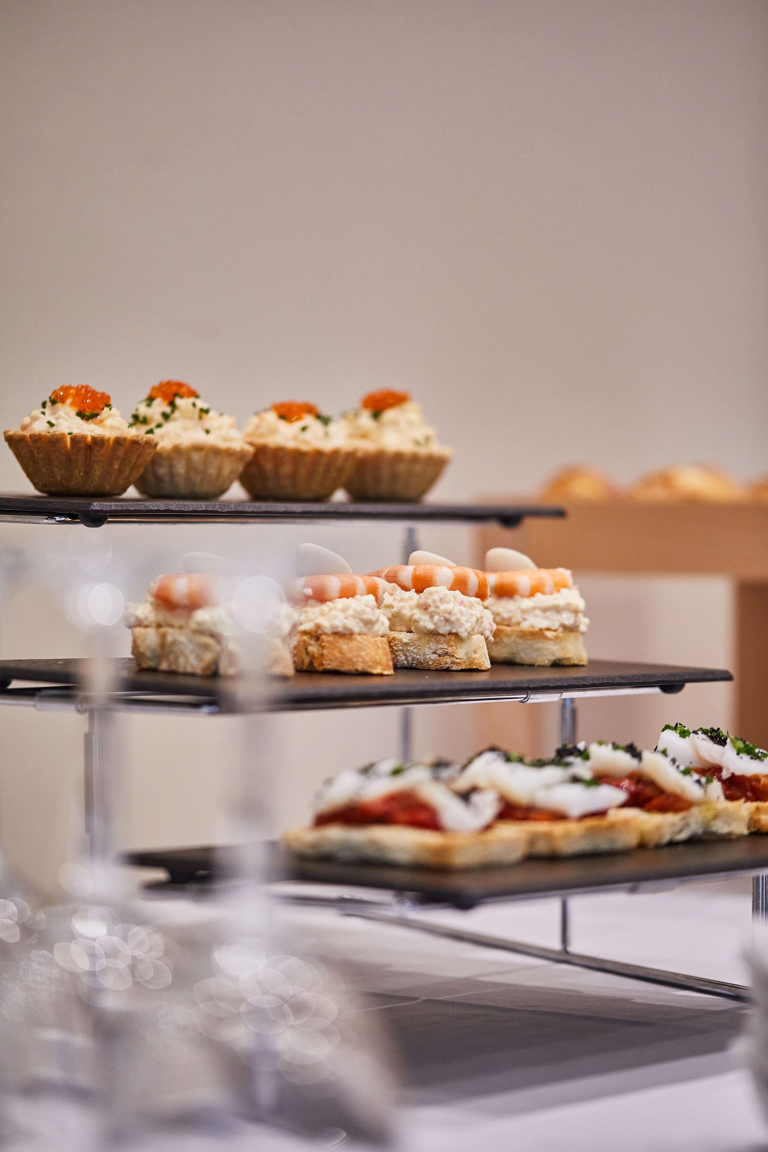 Una presentación escalonada de diversas entradas, entre ellas cupcakes y platos salados, sobre una mesa de vidrio.