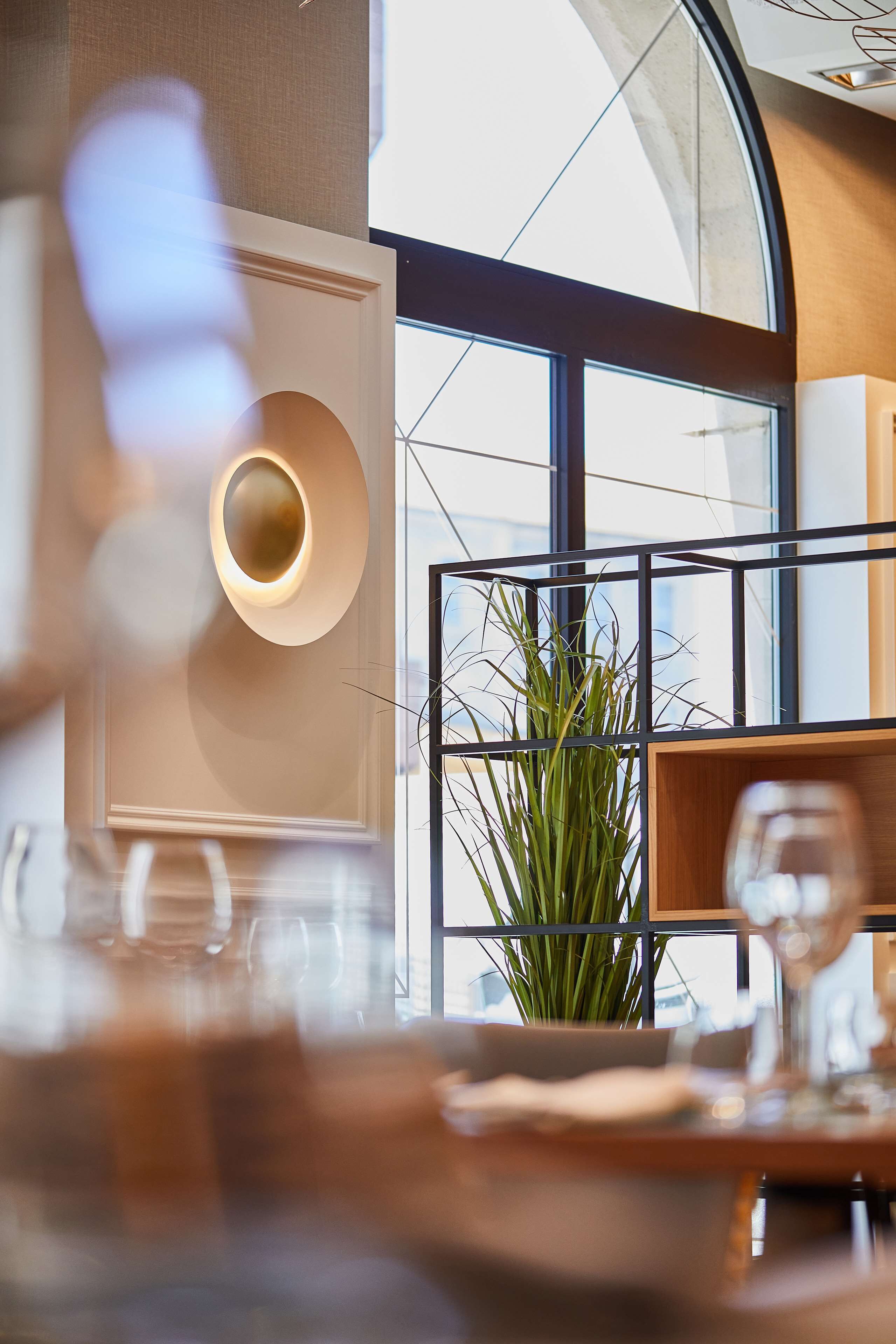 Un espace repas moderne avec une grande fenêtre, une plante en pot et un luminaire contemporain.