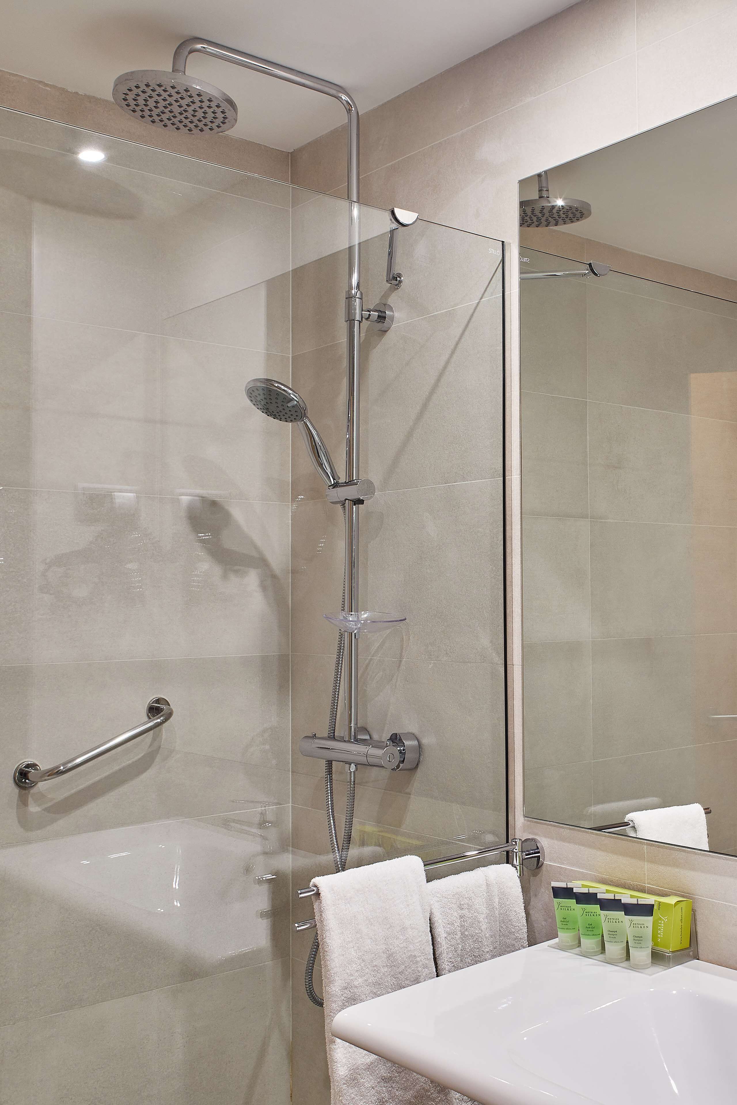 Un baño moderno con ducha envuelta en vidrio, una bañera y un tocador con artículos de aseo.