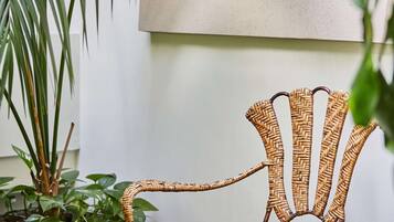 Una silla de mimbre con una mesa de vidrio en una habitación con pared blanca y una planta grande.