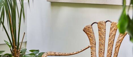 A wicker chair with a glass table in a room with a white wall and a large plant.