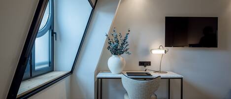 A modern bedroom with a sloped ceiling, a desk with a chair, a bedside table, a bed, and a TV mounted on the wall.