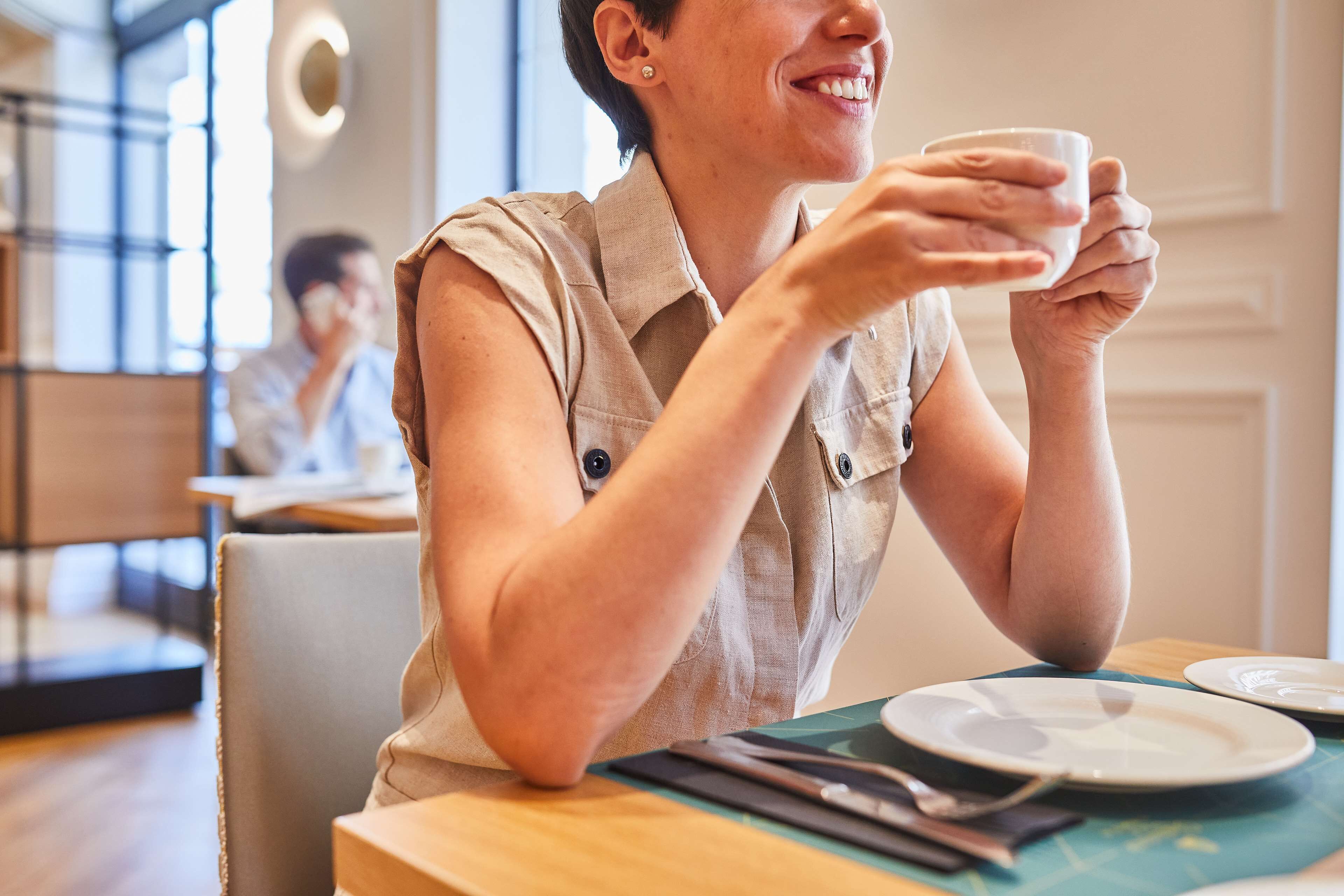 A person seated at a table with a cup, a plate, and cutlery.