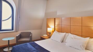 Habitación de hotel con cama, una silla, una mesita y una mesita de noche con lámpara.