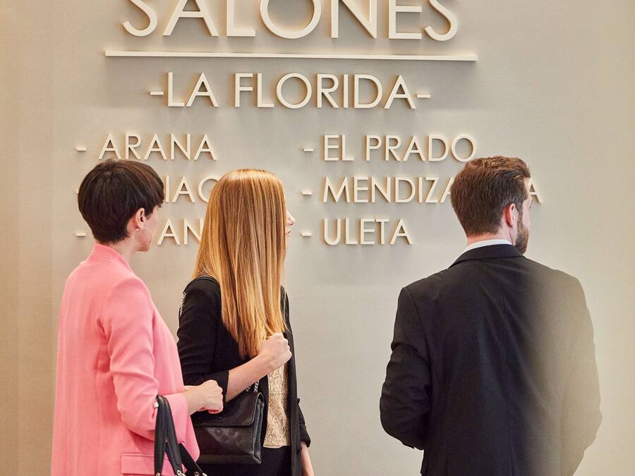 A group of people standing in front of a wall with the text "SALONES - LA FLORIDA - ARANA - EL PRADO - MENDIZAR - ULETA".