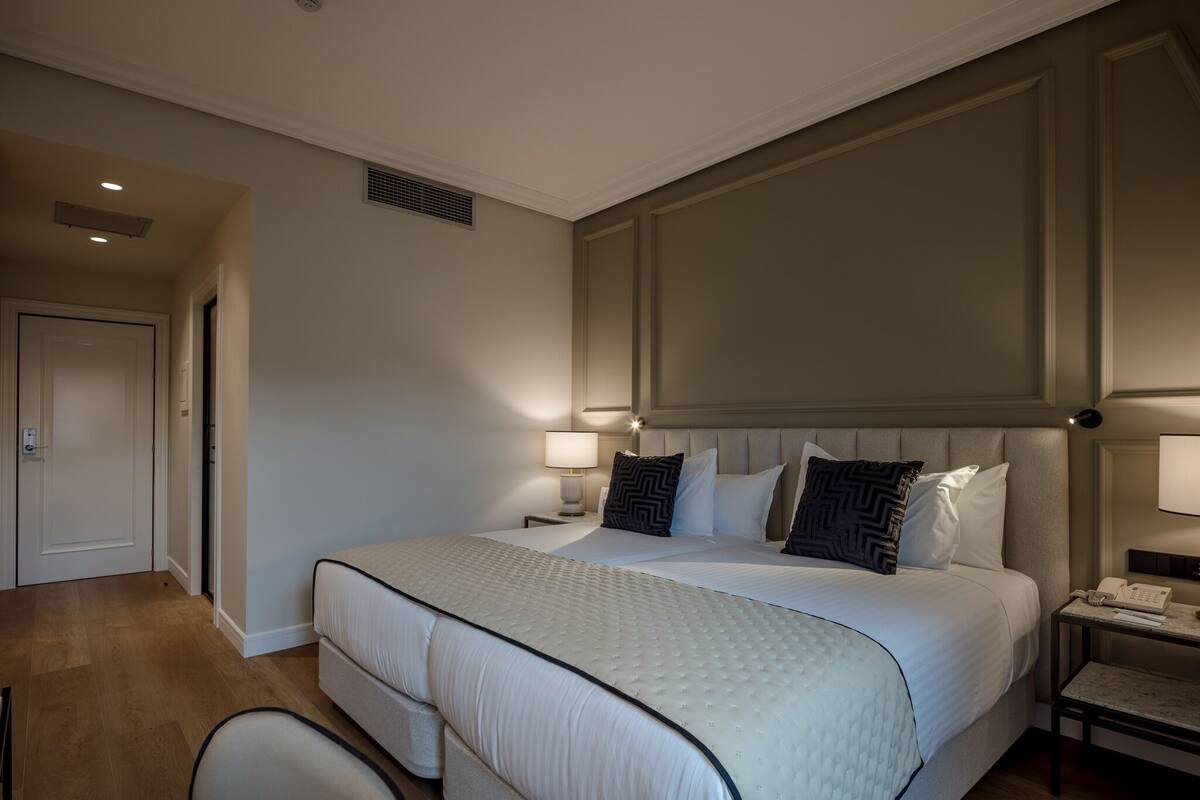 A hotel room with a large bed, two bedside tables, a chair, and a door.