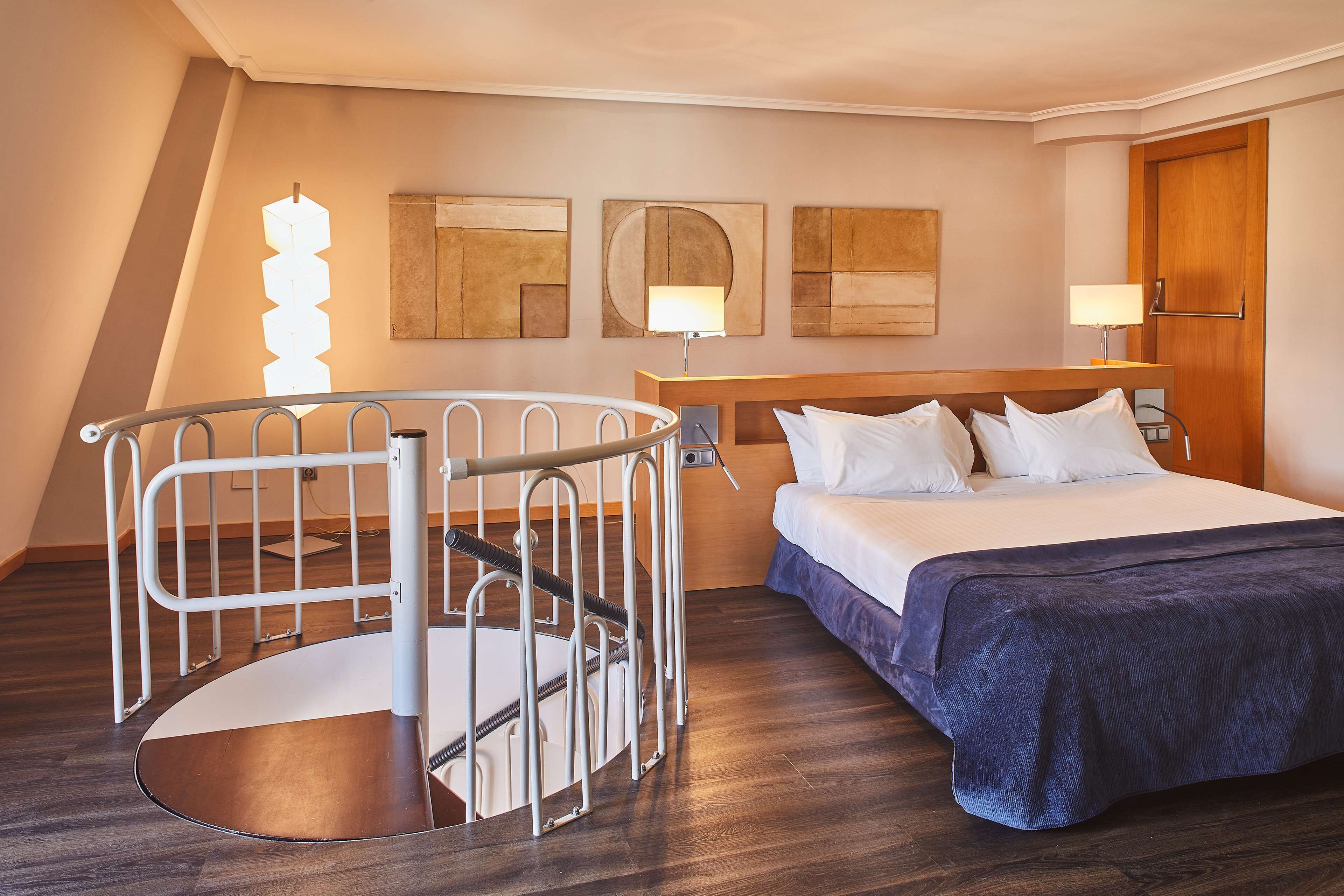 A hotel room with a bed, a desk, and a spiral staircase.