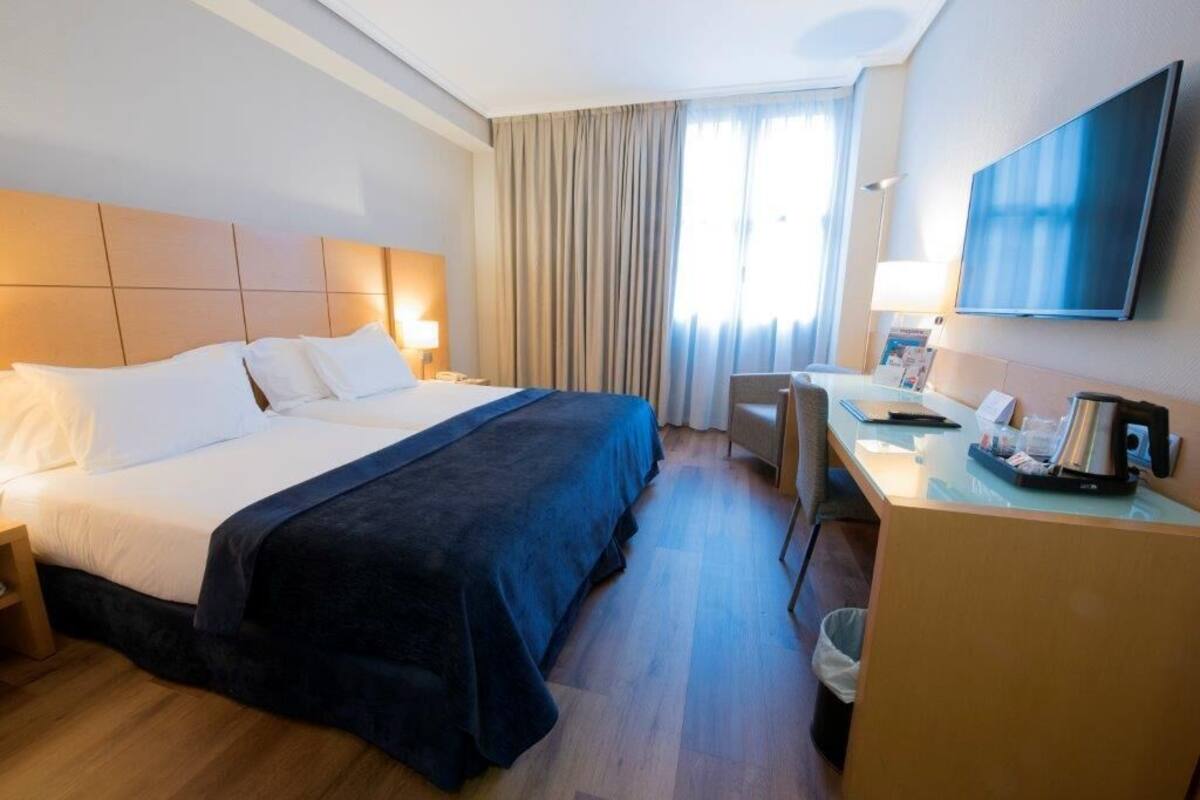 A hotel room with a bed, desk, chair, and a TV.
