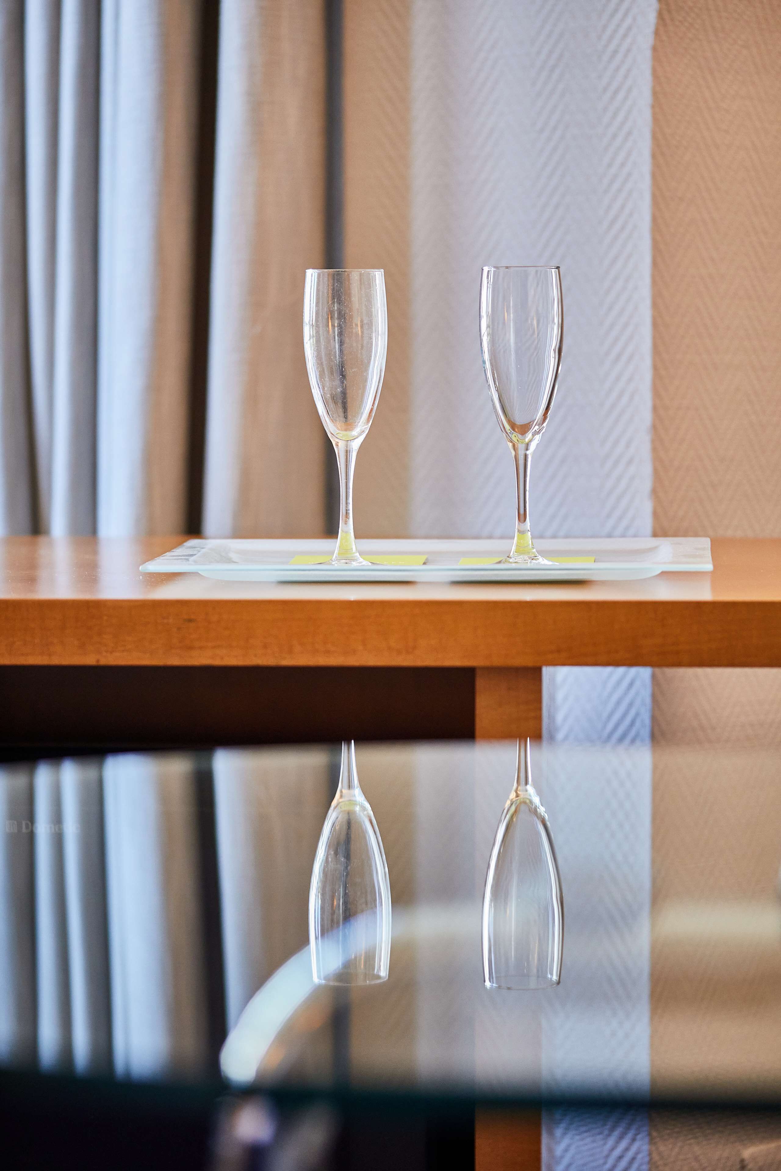 Dos copas de vino vacías sobre una mesa de madera con una superficie reflectante debajo.