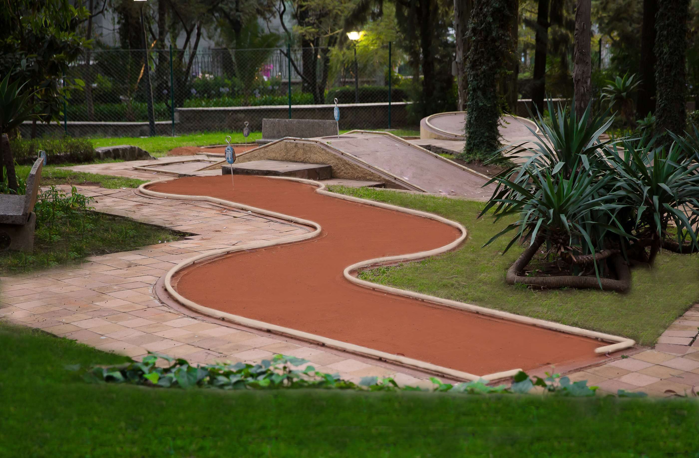 Un campo de mini golf con un sendero serpenteante, una pequeña rampa y una zona verde con plantas.