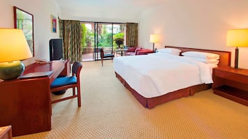 A hotel room with a bed, two bedside tables with lamps, a desk with a chair, a television, and a view of the outdoors through a glass door.