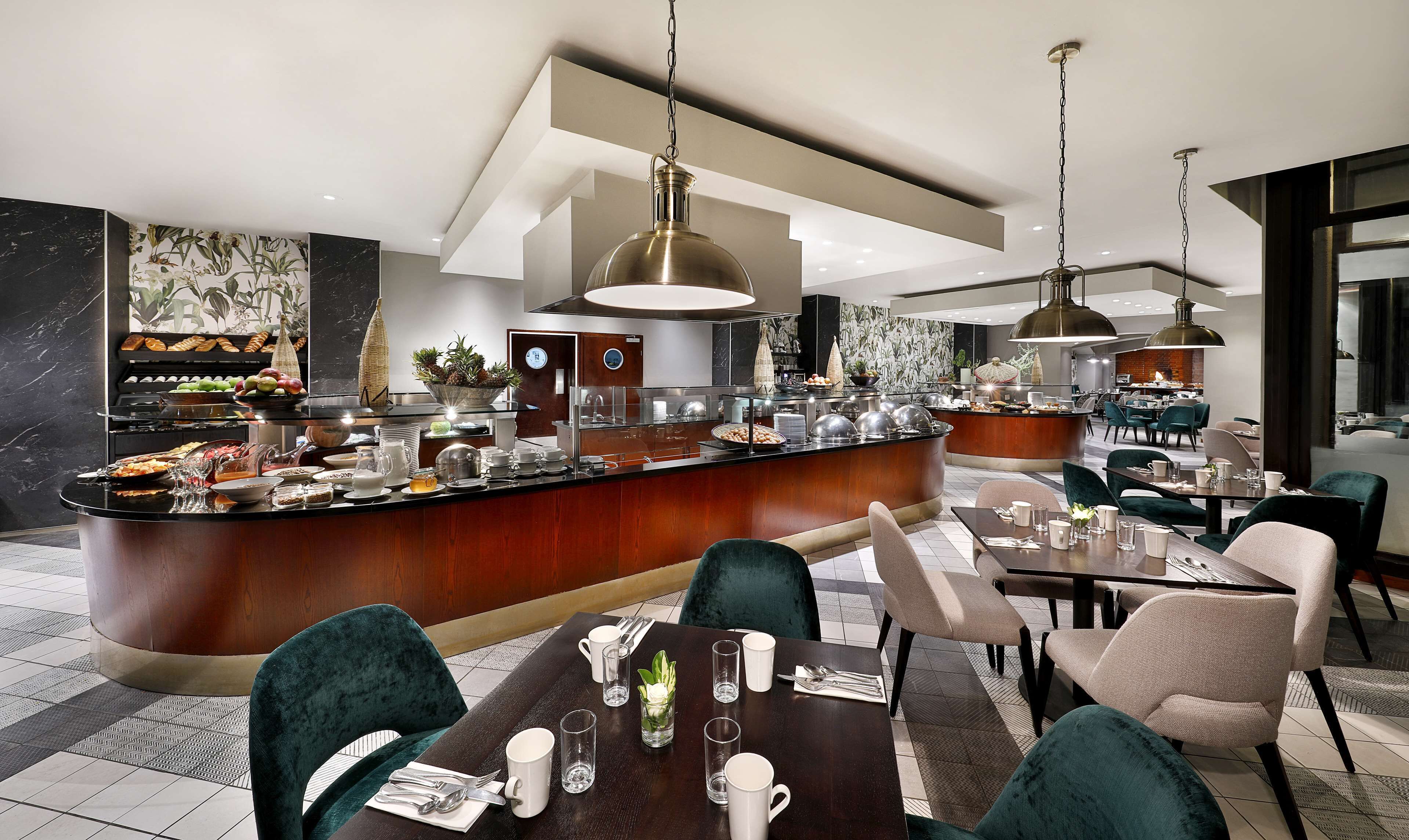 Een moderne eetruimte met een centrale bar, verschillende zithoeken en diverse stations voor eten en drinken.