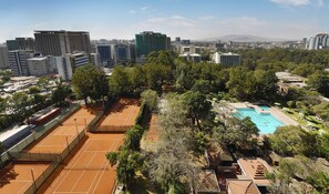 A tennis court surrounded by trees and a swimming pool with lounge chairs. - Hilton Addis Ababa (Addis Ababa)