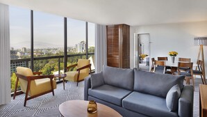 A modern hotel room with a large window offering a city view, a grey sofa, yellow armchairs, a dining table with chairs, and a floor lamp. - Hilton Addis Ababa (Addis Ababa)