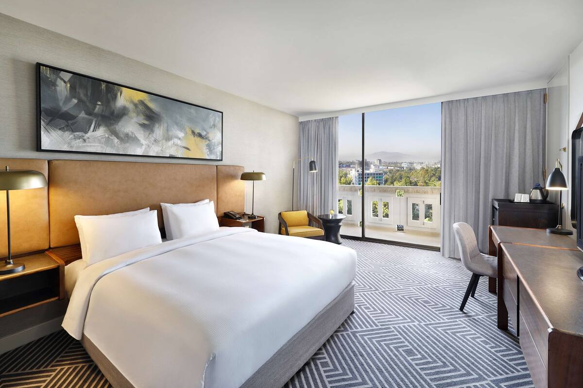 Une chambre d’hôtel avec un grand lit, un bureau, une chaise, une télévision et une vue sur la ville.