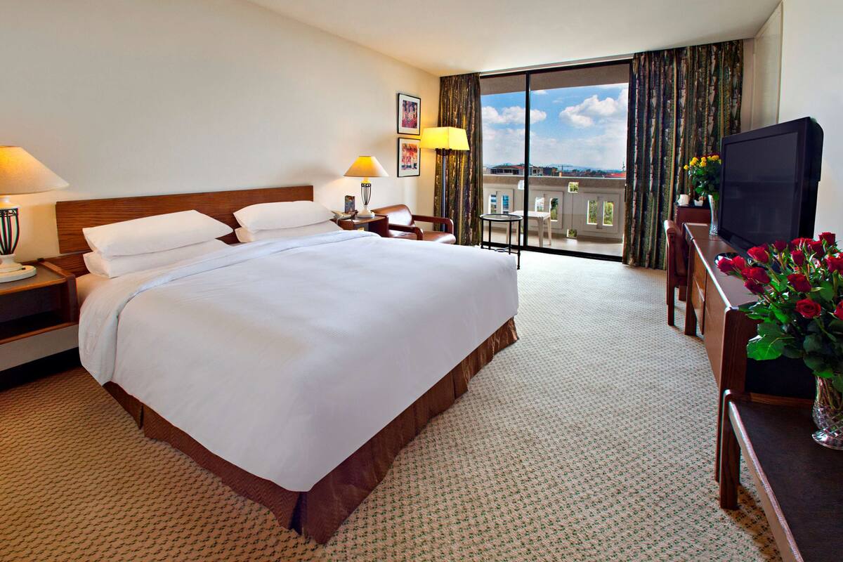 Une chambre d’hôtel avec un grand lit, un bureau avec une télévision, une chaise et un balcon avec vue.