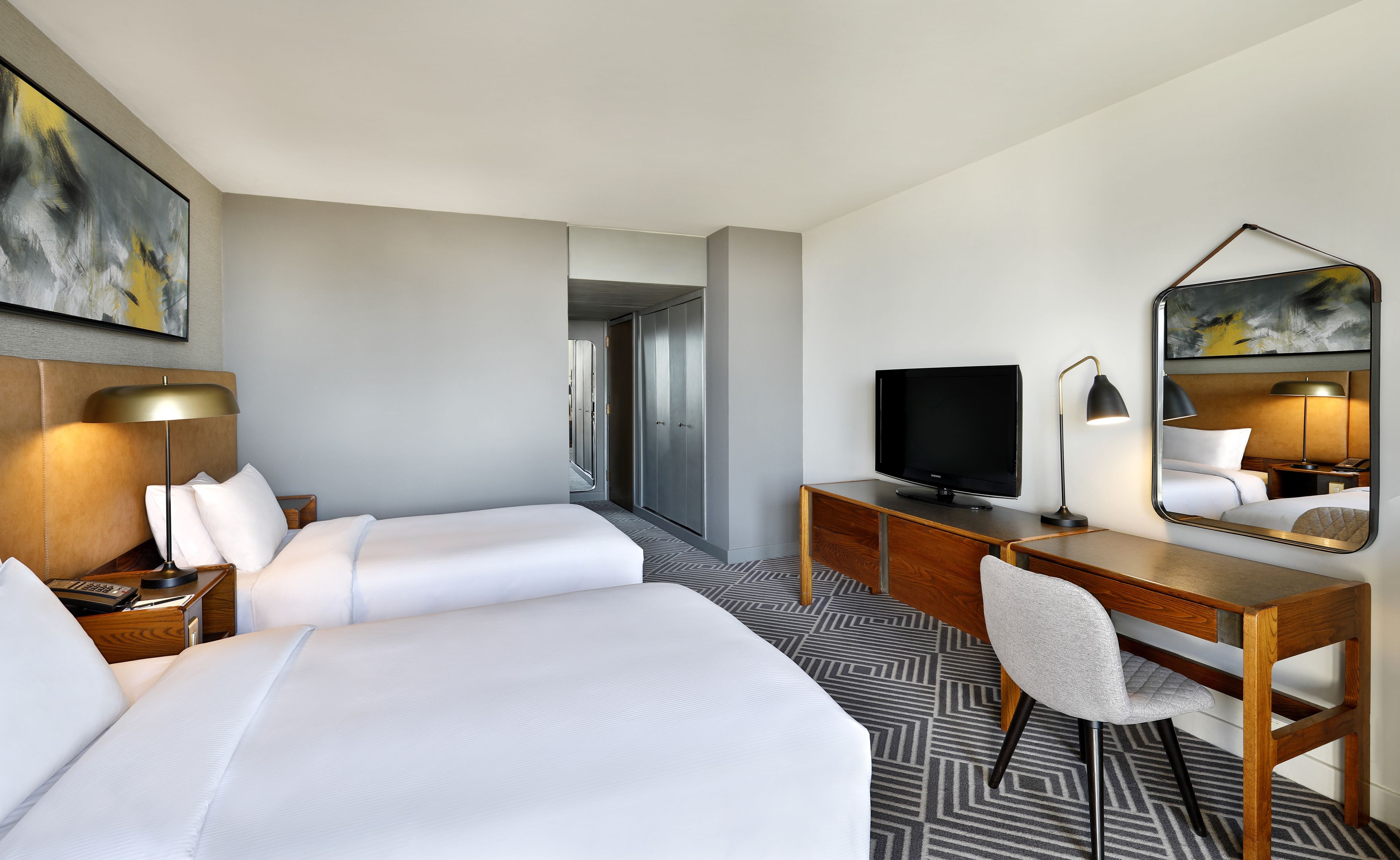 Een hotelkamer met een bed, een bureau, een televisie, een stoel en een spiegel.