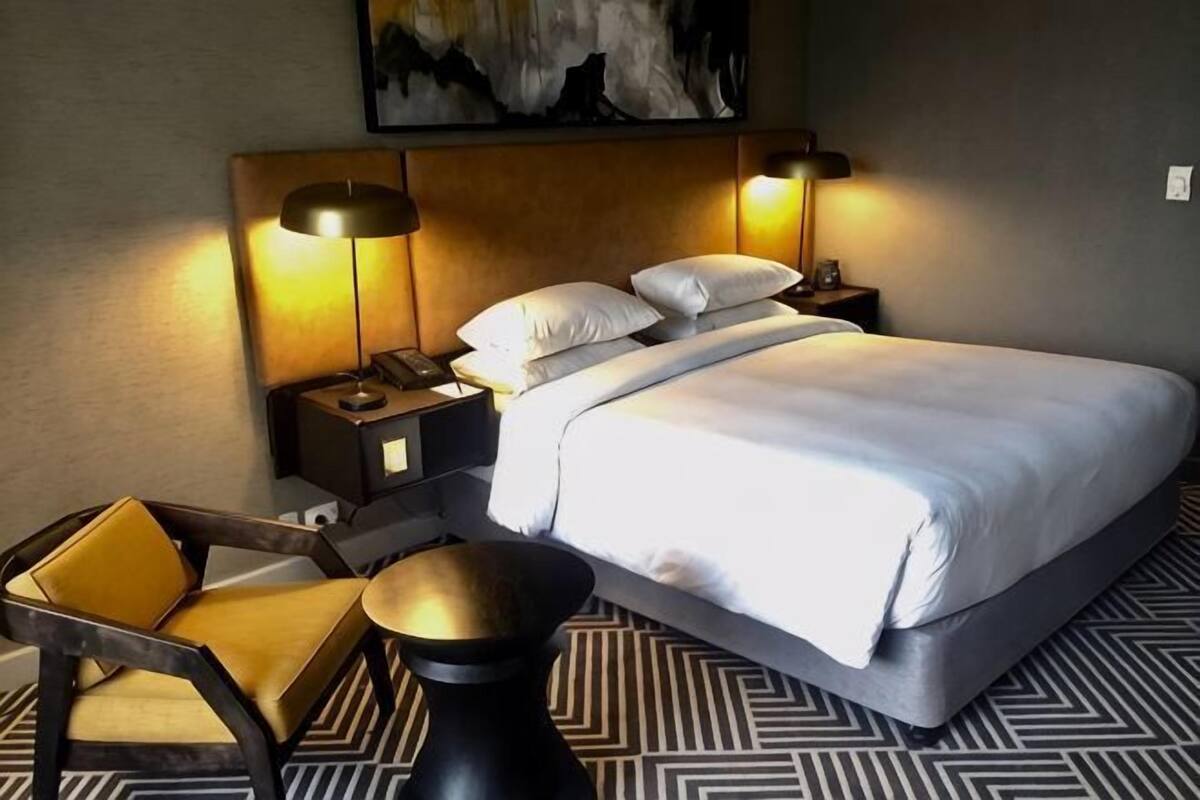 Une chambre d’hôtel avec un lit, deux tables de chevet, une chaise, une petite table et un tableau au mur.