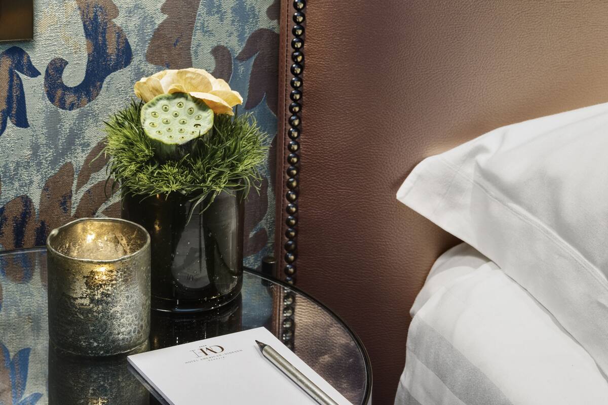 A neatly arranged hotel room with a bed, a glass table with a vase of flowers, a candle, and a menu.
