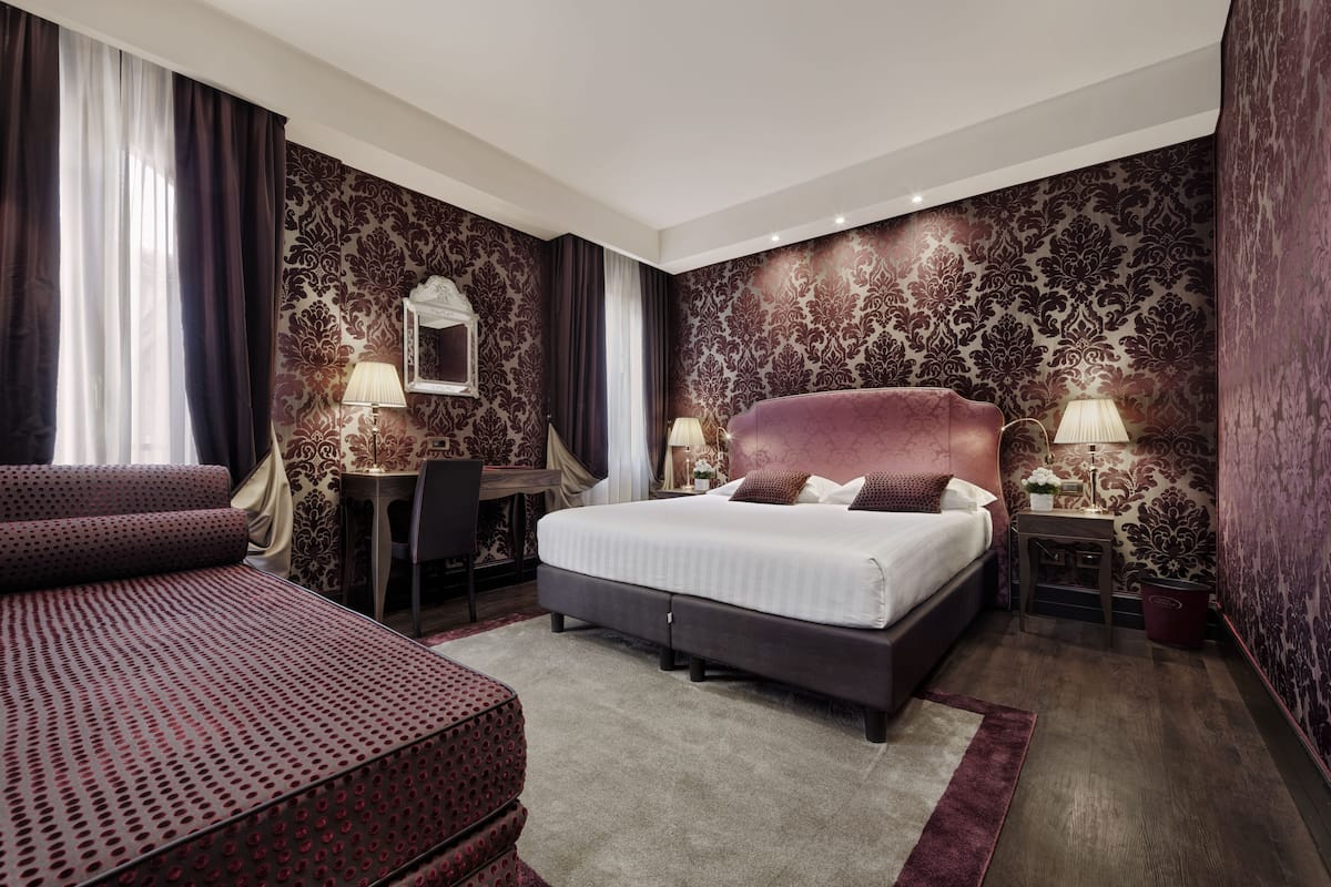 A hotel room with a large bed, a desk, and a sofa.
