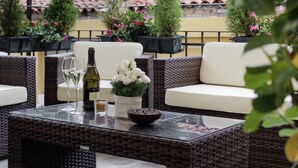An outdoor seating area with wicker furniture and a glass table, featuring a bottle of wine, glasses, and a bowl of flowers. - Hotel American Dinesen (Venice)