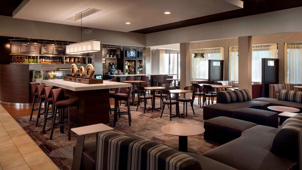 A modern hotel lobby with a bar area, seating arrangements, and a visible menu board.