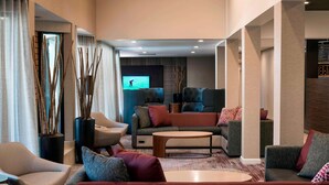 A modern hotel lobby with a sofa, chairs, a coffee table, and a TV screen.