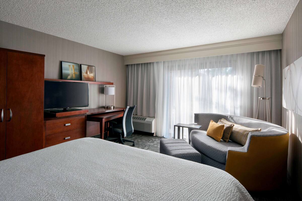 A hotel room with a large bed, a desk with a chair, a sofa, and a television.