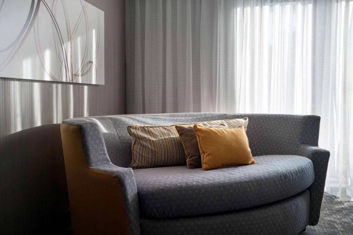A modern living room with a grey sofa, patterned cushions, and a large abstract painting on the wall.