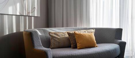 A modern living room with a grey sofa, patterned cushions, and a large abstract painting on the wall.