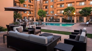 A poolside area with lounge chairs, a pool, and a building with balconies.