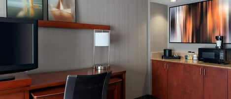 A hotel room with a wooden desk, a chair, a flat-screen TV, a lamp, a microwave, and a large abstract painting on the wall.