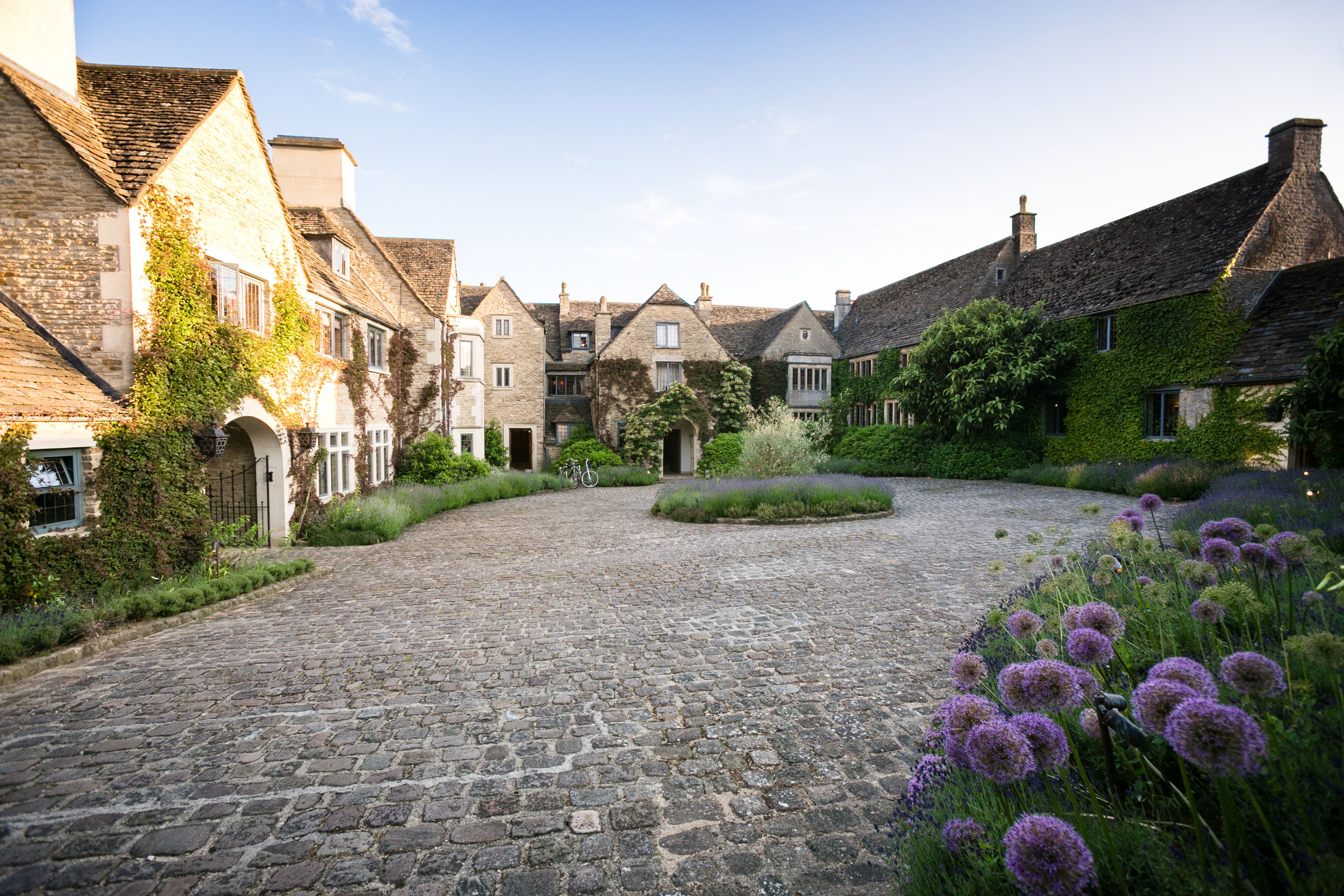 A cobblestone street lined with historic buildings, a central garden, and a bicycle parked in the distance.