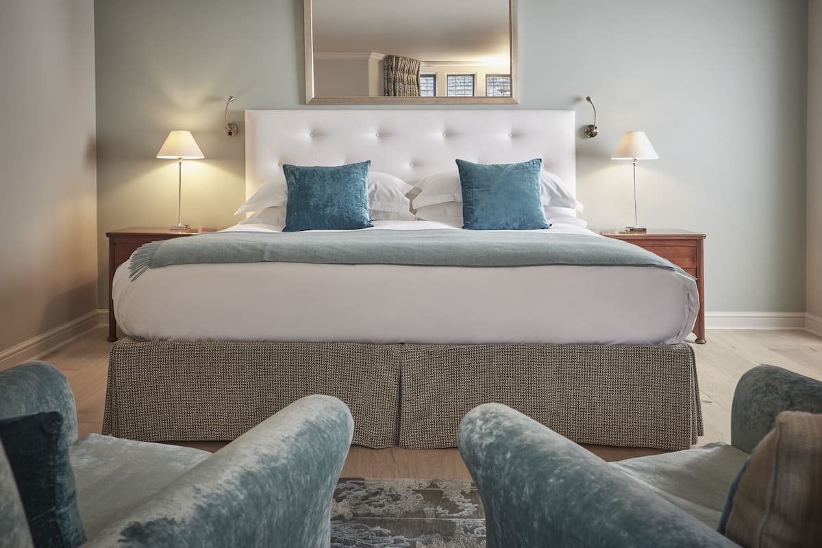 A neatly arranged bedroom with a large bed, two bedside lamps, a mirror above the bed, and a patterned rug on the floor.
