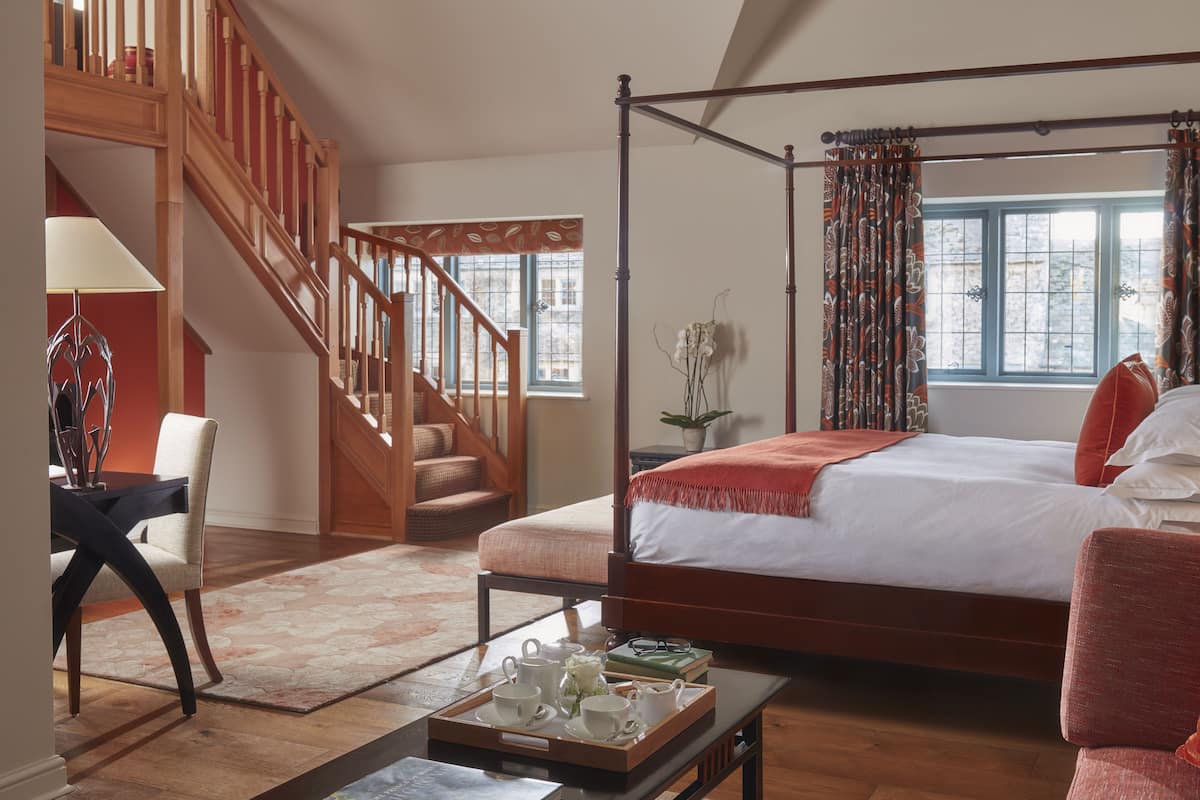 A spacious bedroom with a four-poster bed, a wooden staircase, and a view of the outdoors.