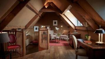 Quarto no sótão com vigas de madeira, uma escrivaninha, cadeiras e uma poltrona vermelha.