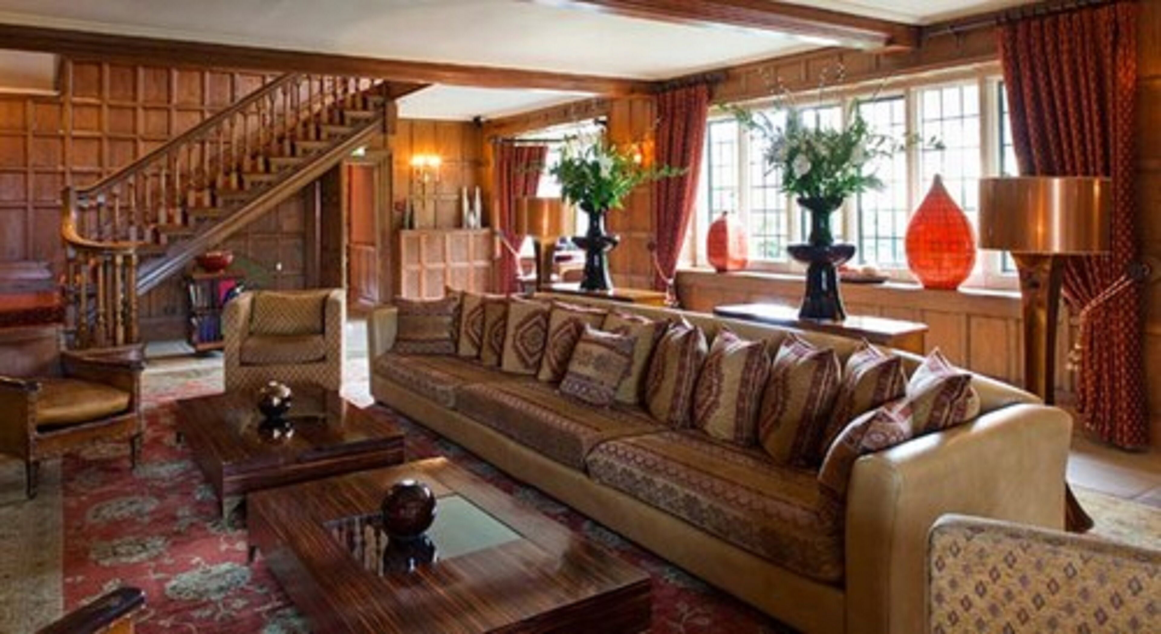 Ein geräumiges Wohnzimmer mit einer großen Couch, einer Holztreppe und einem großen Fenster mit Vorhängen.