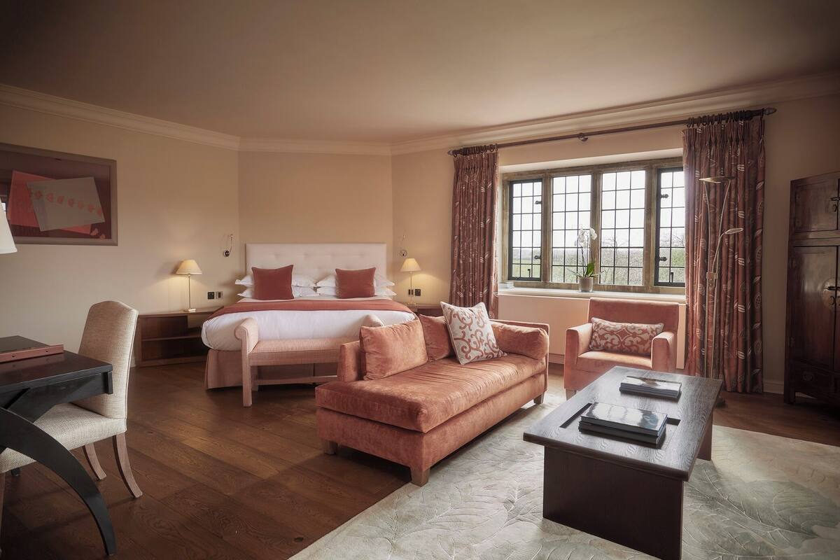 A hotel room with a bed, two sofas, a coffee table, a desk, and a window with curtains.