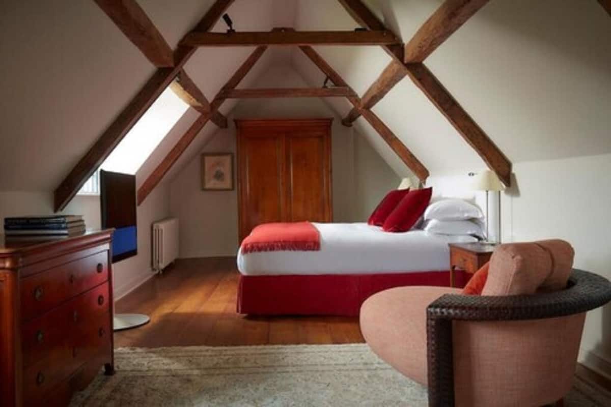 A bedroom with a bed, dresser, chair, and wooden beams on the ceiling.