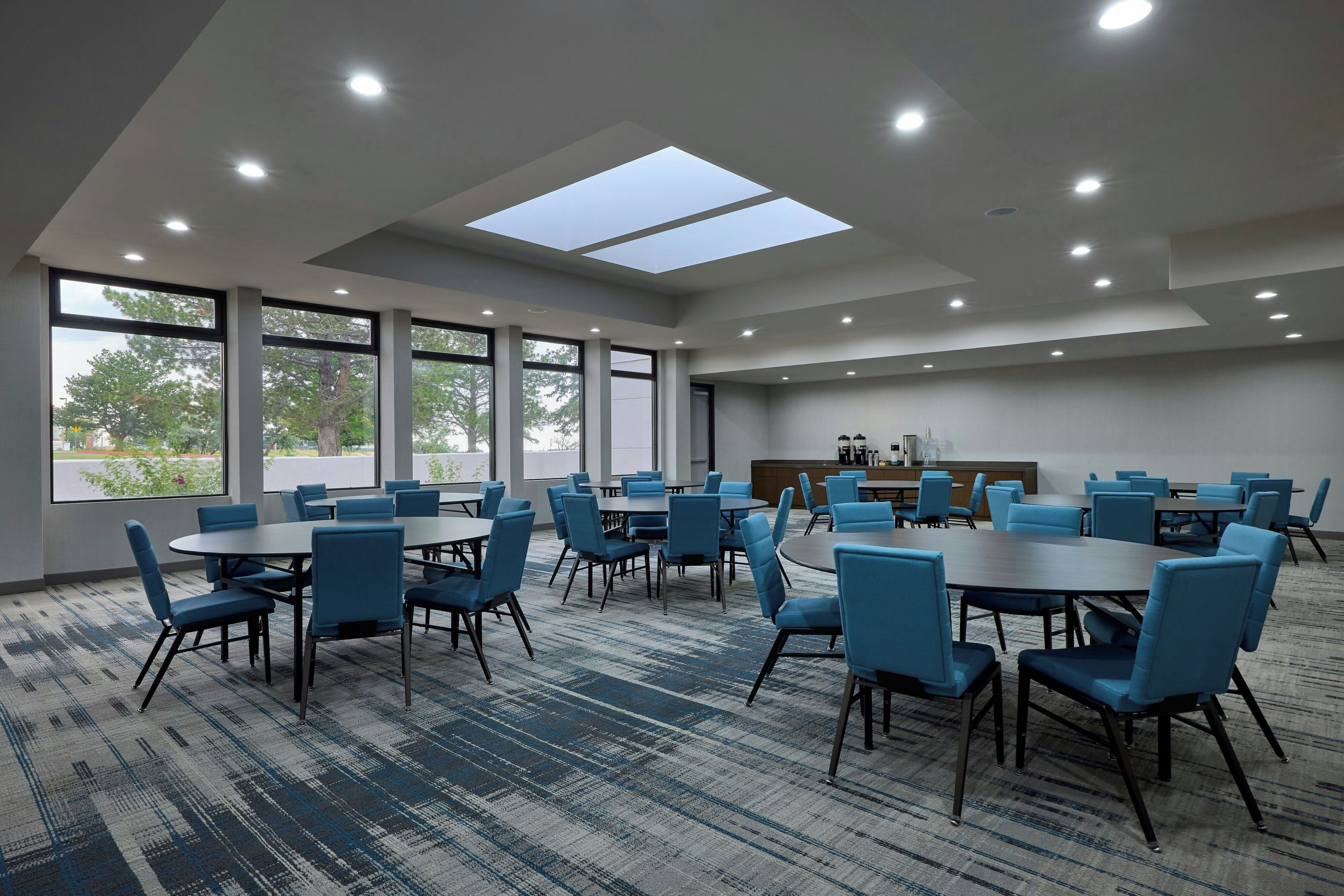 A conference room with multiple tables and chairs, large windows, and a skylight.