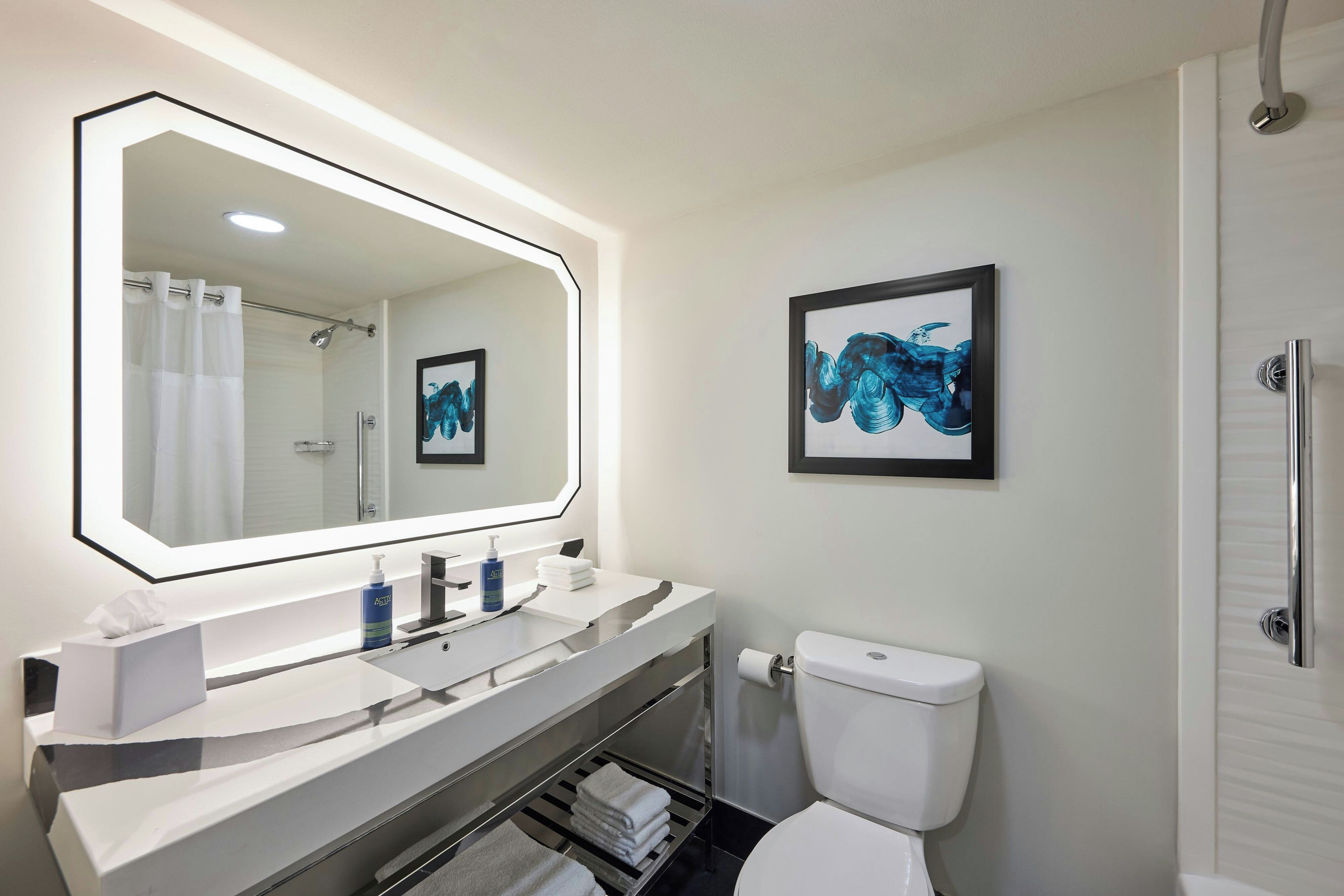 A modern bathroom with a large mirror, a toilet, a sink with a towel rack, and a shower.