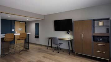 A modern office space with a desk, two bar stools, a chair, a TV, a cabinet with drawers, and a microwave.