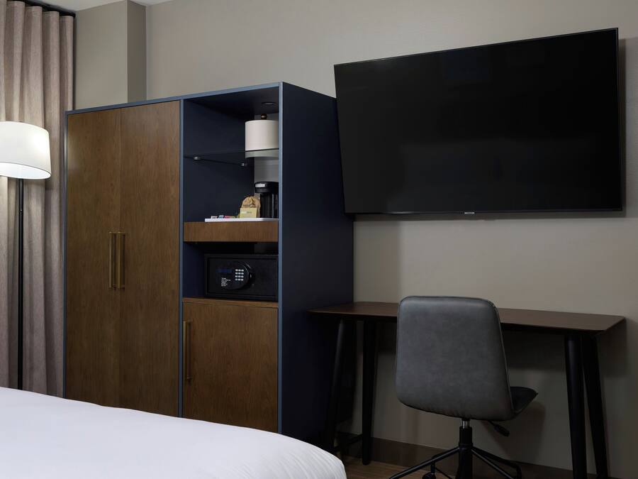 A hotel room with a bed, a wardrobe, a desk, a chair, a television, and a lamp.