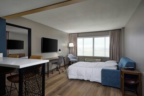 Habitación de hotel con cama, escritorio, silla, televisor y ventana con cortinas.
