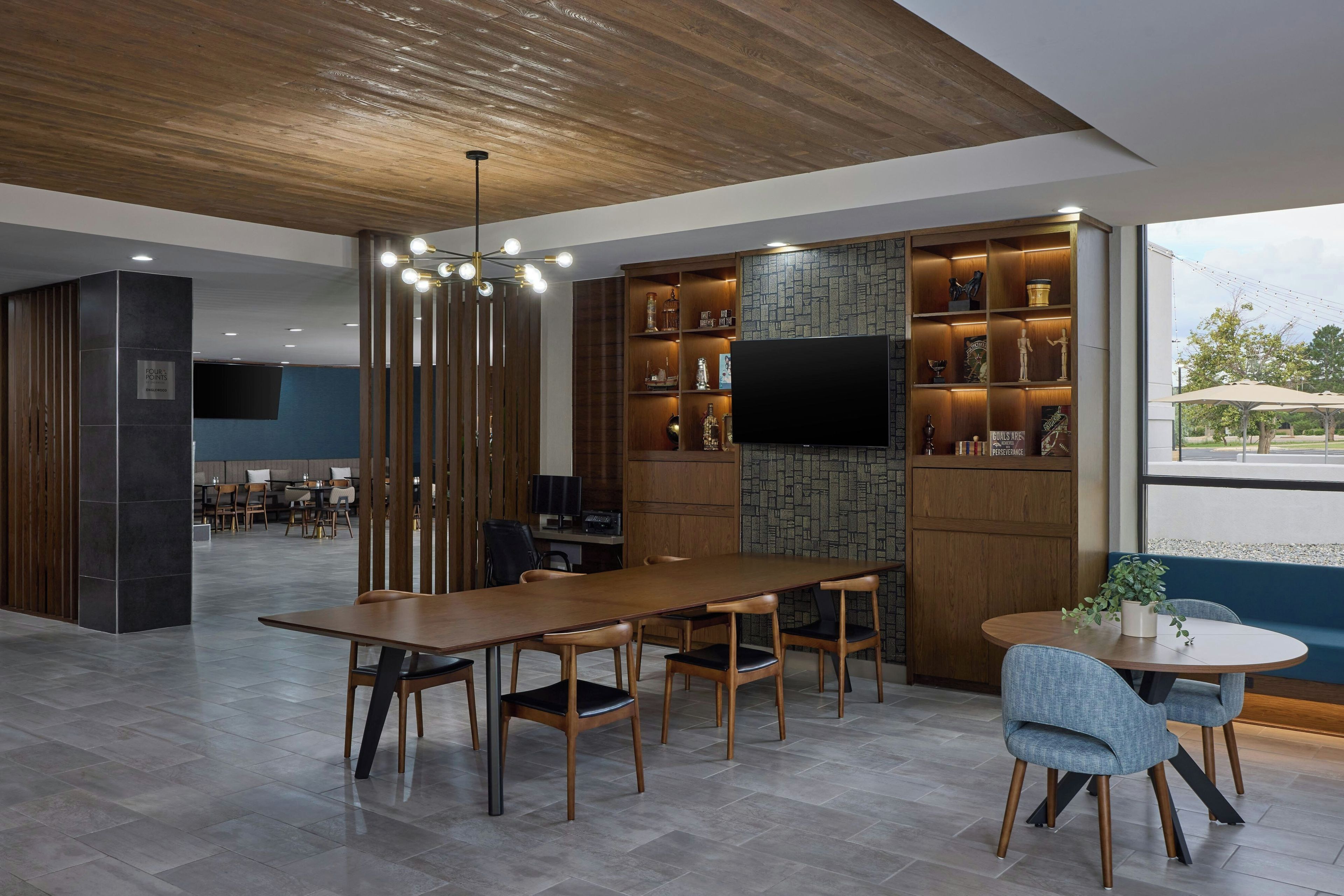 A modern conference room with a long table, chairs, a TV, and a bookshelf with various items.