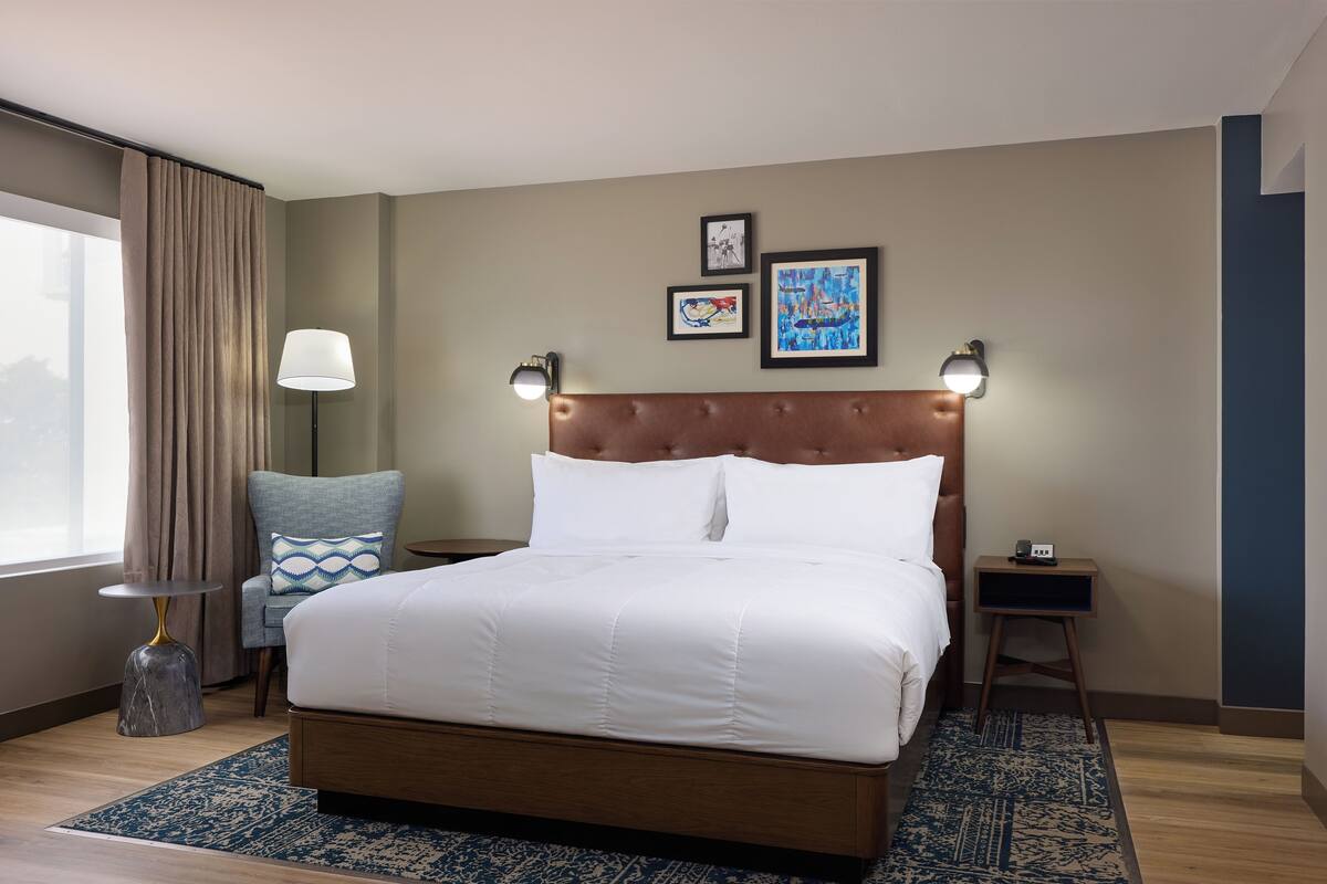 A neatly arranged hotel room with a large bed, a side table with a lamp, and artwork on the wall.